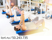 Men and women practicing pilates with roller on gray mat in gym room. Стоковое фото, фотограф Яков Филимонов / Фотобанк Лори