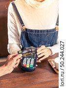 Close-up of asian customer using his credit card with contactless nfs technology to pay a barista for his coffee purchase at a cafe bar. Стоковое фото, агентство Ingram Publishing / Фотобанк Лори