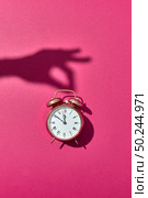 Retro alarm clock painted golden with hard shadows from woman’s hand holding it on a hot pink background, copy space.. Hand’s shadows holds retro golden painted alarmclock. Стоковое фото, агентство Ingram Publishing / Фотобанк Лори