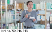 Selective young woman holding pills and box of medicine for purchase in drugstore. Стоковое видео, видеограф Яков Филимонов / Фотобанк Лори
