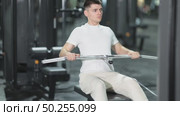 In gym, young man uses cable row machine to strengthen arm muscles. Стоковое видео, видеограф Яков Филимонов / Фотобанк Лори