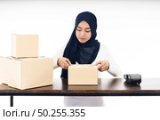 Asian muslim women merchant working with laptop computer from home on wooden table with postal parcel cardboard boxes preparing for shipping her order. Studio shot on white background using as Selling online and small business SME ideas concept. Стоковое фото, агентство Ingram Publishing / Фотобанк Лори