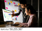 Young adult asian businessman dicuss with collegue about work with analysis graph on white board late at night in their office with desktop computer. Using as hard working and working late concept. Стоковое фото, агентство Ingram Publishing / Фотобанк Лори