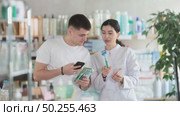Positive young guy buyer at pharmacy choosing best toothbrush, scan QR code, young girl pharmacist consulting and offering variety of goods to customer. Стоковое видео, видеограф Яков Филимонов / Фотобанк Лори