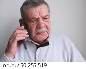 Elderly man is talking on a smartphone. A tired, distrustful, shocked pensioner who feels uncomfortable listening to an unknown caller making questionable requests. Стоковое фото, фотограф Терехова Марина / Фотобанк Лори