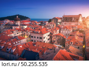 Aerial view of houses with red roofs at sunset in Dubrovnik, Croatia. Top view of beautiful architecture in european old city. City lights, historical centre, buildings and blue sky at dusk in summer. Стоковое фото, агентство Ingram Publishing / Фотобанк Лори