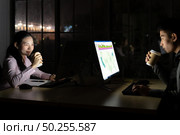 Young adult asian businessman and woman drinking hot cofee while working late at night in their office with desktop computer and laptop. Using as hard working and working late concept. Стоковое фото, агентство Ingram Publishing / Фотобанк Лори