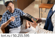 Asian customer using credit card with EMV chip technology to pay a waitress for coffee purchase at table in cafe. Стоковое фото, агентство Ingram Publishing / Фотобанк Лори