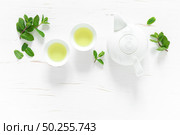 Green mint tea with fresh leaves in cups and teapot overhead on white wooden table, healthy warming drink, antioxidant beverage, top view. Стоковое фото, агентство Ingram Publishing / Фотобанк Лори