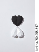 Valentine’s holiday card with two plaster hearts white and black on a light gray background with hard shadows, copy space. Top view. Valentine’s day greeting card.. Two gypsum hearts black and white with shadows. Стоковое фото, агентство Ingram Publishing / Фотобанк Лори