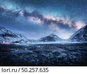 Milky Way above snow covered mountains and stone beach in winter at night in Lofoten Islands, Norway. Arctic landscape with blue starry sky,  sea coast, snowy rocks, galaxy. Beautiful space and nature. Стоковое фото, агентство Ingram Publishing / Фотобанк Лори