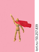 Movable miniature articulation mannequin in a red cape is flying up with raised hand as a superhero or superman against pink background, copy space. Business success and leadeship concept.. Wooden mannequin miniature doll in a red cape flies up as a superman. Стоковое фото, агентство Ingram Publishing / Фотобанк Лори