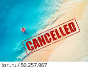 Travel and holidays cancelled due to epidemic of coronavirus. Tourism and resort cancelation due to Covid-19. Aerial view of beautiful young woman with pink donut swim ring on the beach, sea and text. Стоковое фото, агентство Ingram Publishing / Фотобанк Лори