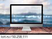 Computer monitor with sea blurred image on a wooden table against the same background with bokeh, copy space. Working remotely at seacoast, on nature, outside office concept.. Computer display with blurred sea background. Стоковое фото, агентство Ingram Publishing / Фотобанк Лори