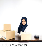 E-Commerce asian muslim women merchant work from home on wooden table with postal parcel cardboard boxes for shipping orders. Studio shot on white background for Selling online and small business SME. Стоковое фото, агентство Ingram Publishing / Фотобанк Лори