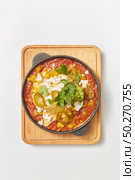 Middle eastern traditional dish Shakshuka from fried eggs with tomatoes, bell pepper, vegetables and herbs in a pan on a wooden board on a light grey background, copy space. Top view.. Shakshuka dish with pita bread in a pan on a wooden board. Стоковое фото, агентство Ingram Publishing / Фотобанк Лори