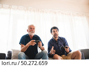 Happy two age generations men family old father embracing young grown adult son having fun enjoying video game. Стоковое фото, агентство Ingram Publishing / Фотобанк Лори