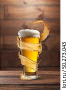 Creative flying spiral yellow splash aroung full glass of fresh cold light beer on a wooden table against wall from wood, copy space.. Glass of light fresh beer with flying spiral splash around mug. Стоковое фото, агентство Ingram Publishing / Фотобанк Лори