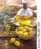 A vibrant still life image of olive oil in a glass bottle and juicy yellow olives in a wooden bowl against a rustic wooden table. The composition is complemented by twigs with small yellow berries and soft sunlight, creating an atmosphere of coziness, warmth and naturalness. Ideal for themes related to healthy eating, Mediterranean cuisine, gastronomy, natural products and cooking. Стоковое AI-изображение, AI-художник Анна Кривицкая / Фотобанк Лори
