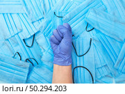 Woman’s hand with clenched fist in a rubber protective glove on a background from medical protective antibacterial face blue masks. Concept of prevention from respiratory sickness and viruses.. Woman clenched fist in a rubber protective glove on a medical masks backgound. Стоковое фото, агентство Ingram Publishing / Фотобанк Лори