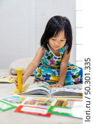 Asian girl child reading interactive book in living room at home as home schooling while city lockdown because of covid-19 pandemic across the world. Home Scholling prepare for Preschool concept. Стоковое фото, агентство Ingram Publishing / Фотобанк Лори