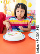 Asian girl kid cutting her birthday cake celebrate with mom alone because city lockdown while COVID-19 Pandemic. Celbration and quarantine concept. Стоковое фото, агентство Ingram Publishing / Фотобанк Лори