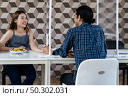 Asian young couple eating out together at new normal social distance restaurant with table shield partition reduce infection of coronavirus covid-19 pandemic. Restaurant new normal lifestyle. Стоковое фото, агентство Ingram Publishing / Фотобанк Лори