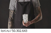 Man barista in a black apron is preparing cooling ice coffee drink with cubes and milk on a black background. Process step by step.Slow motion, Full HD video, 240fps, 1080p.. Cooking process of cold fresh ice coffee drink with milk by barista. Стоковое фото, агентство Ingram Publishing / Фотобанк Лори