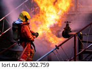 Firefighter using water fog type fire extinguisher to fighting with the fire flame from oil pipeline leak and explosion on oil rig and natural gas station. Firefighter and industrial safety concept. Стоковое фото, агентство Ingram Publishing / Фотобанк Лори