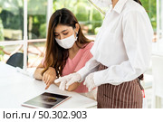 Asian waitress wear facemask and face shield using tablet to show restaurant electronic menu and recommend to customer. New normal technology and lifestyle food and dining concept. Стоковое фото, агентство Ingram Publishing / Фотобанк Лори