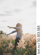 Young beautiful woman standing stretch her arms in the air on the grass field. Woman enjoy with nature during sunset. Стоковое фото, агентство Ingram Publishing / Фотобанк Лори