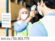 Islam asian warehouse worker take temperature to worker before getting in factory after reopening after city lockdown from COVID-19 coronavirus pandemic in warehouse distribution center environment. Стоковое фото, агентство Ingram Publishing / Фотобанк Лори