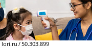 Panoramic Asian female doctor use infrared thermometer to take temperature to little girl child in living room while doctor visit at home. Home health care delivery and doctor visiting concept. Стоковое фото, агентство Ingram Publishing / Фотобанк Лори