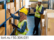 Islam Muslim female warehouse worker do logistic inventory route with his manager use walky talky inbackground in warehouse distribution. For business warehouse inventory and logistic concept. Стоковое фото, агентство Ingram Publishing / Фотобанк Лори