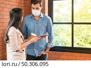 Two business person standing for brainstorm and discuss their work with digital tablet. They wear protective face mask in new normal office preventing coronavirus COVID-19 spreading. Стоковое фото, агентство Ingram Publishing / Фотобанк Лори