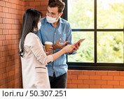 Two business person standing for brainstorm and discuss their work with digital tablet. They wear protective face mask in new normal office preventing coronavirus COVID-19 spreading. Стоковое фото, агентство Ingram Publishing / Фотобанк Лори