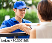 Asian woman sign electronic signature to portable mobile device after receive package from male delivery man in blue shirt. Package shopping delivery and digital sign concept. Стоковое фото, агентство Ingram Publishing / Фотобанк Лори