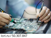 Closeup shot of male hands testing electric current voltage in circuit board of disassembled laptop using multimeter tool on table in maintenance shop. Стоковое фото, агентство Ingram Publishing / Фотобанк Лори