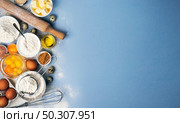 Baking ingredients for dough on blue background, top view of flour, eggs, butter, sugar and kitchen utensils for homemade baking with copy space for text. Baking ingredients on blue color background, top view. Стоковое фото, агентство Ingram Publishing / Фотобанк Лори