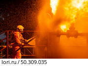 Firefighter using water fog type fire extinguisher to fighting with the fire flame from oil pipeline leak and explosion on oil rig and natural gas station. Firefighter and industrial safety concept. Стоковое фото, агентство Ingram Publishing / Фотобанк Лори