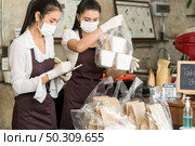 Asian waitress wear protective face mask prepare food for takeout and curbside pickup orders while city lockdown from coronavirus COVID-19 pandemic. This is essential service while lockdown. Стоковое фото, агентство Ingram Publishing / Фотобанк Лори