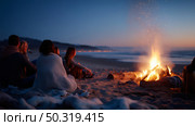 Friends gather around a warm bonfire on the beach during twilight, enjoying a relaxed evening by the ocean. Стоковое AI-изображение, AI-художник Сергей Толмачёв / Фотобанк Лори