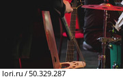 A musician plays double bass on a dimly lit stage. In the background on a stand a bass guitar and a drummer behind a drum kit. Стоковое видео, видеограф Воловодов Владимир / Фотобанк Лори