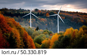beauty of fall foliage surrounding two towering wind turbines near showcasing the harmony between nature and renewable energy. The concept of an alternative energy source, energy saving, and careful attitude towards our planet Earth. Стоковое AI-изображение, AI-художник ALLA YURTAYEVA / Фотобанк Лори