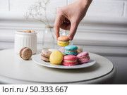 hand picking up macaroon from white plate kept white table. Стоковое фото, агентство Ingram Publishing / Фотобанк Лори