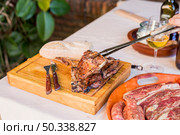 person holding fresh grilled beef steak with tong wooden board. Стоковое фото, агентство Ingram Publishing / Фотобанк Лори