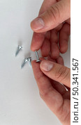 Close-up of hands and metal screws on a white surface, focusing on one bolt between fingers. Стоковое фото, фотограф Анастасия / Фотобанк Лори