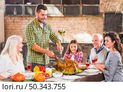 young man cutting baked chicken table with family. Стоковое фото, агентство Ingram Publishing / Фотобанк Лори