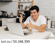 man home during pandemic showing thumbs up during video call laptop. Стоковое фото, агентство Ingram Publishing / Фотобанк Лори