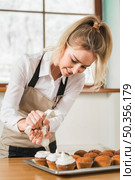female baker decorating cupcake with white butter cream by squeezing icing bag. Стоковое фото, агентство Ingram Publishing / Фотобанк Лори